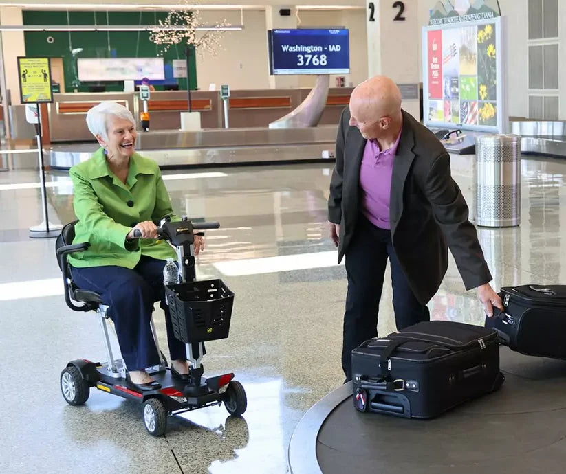 Senior woman riding Buzzaround CarryOn mobility scooter at airport baggage claim with man handling luggage