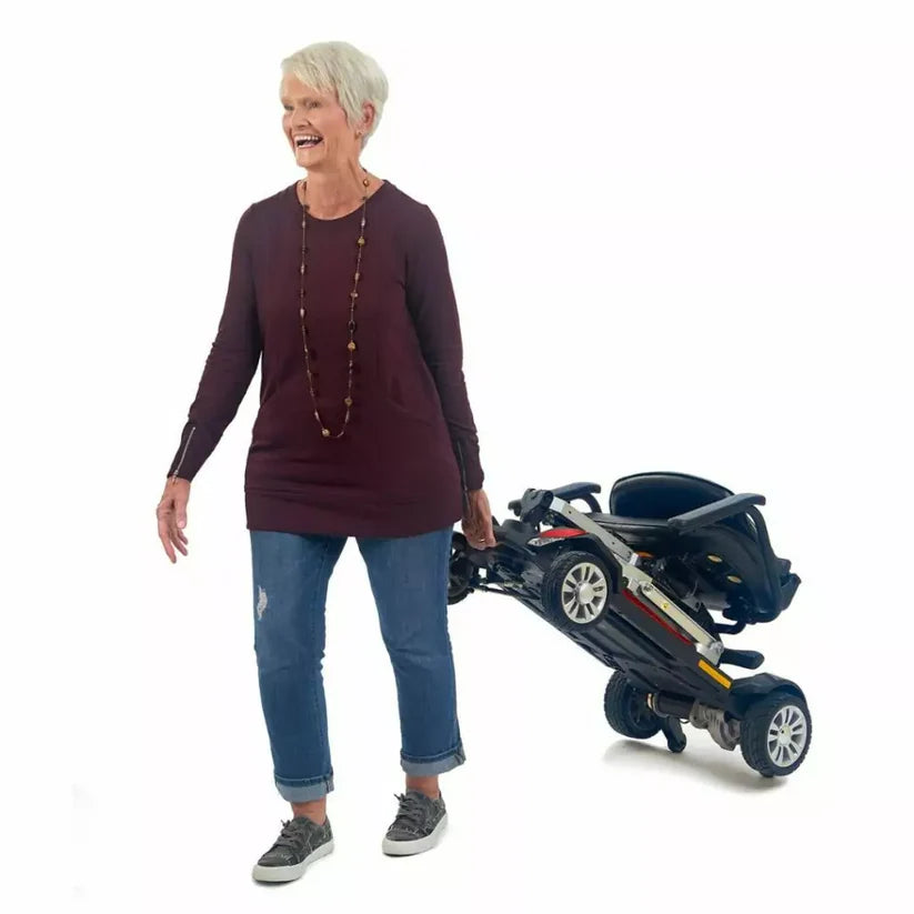 Senior woman carrying folded Buzzaround CarryOn mobility scooter by Golden Technologies