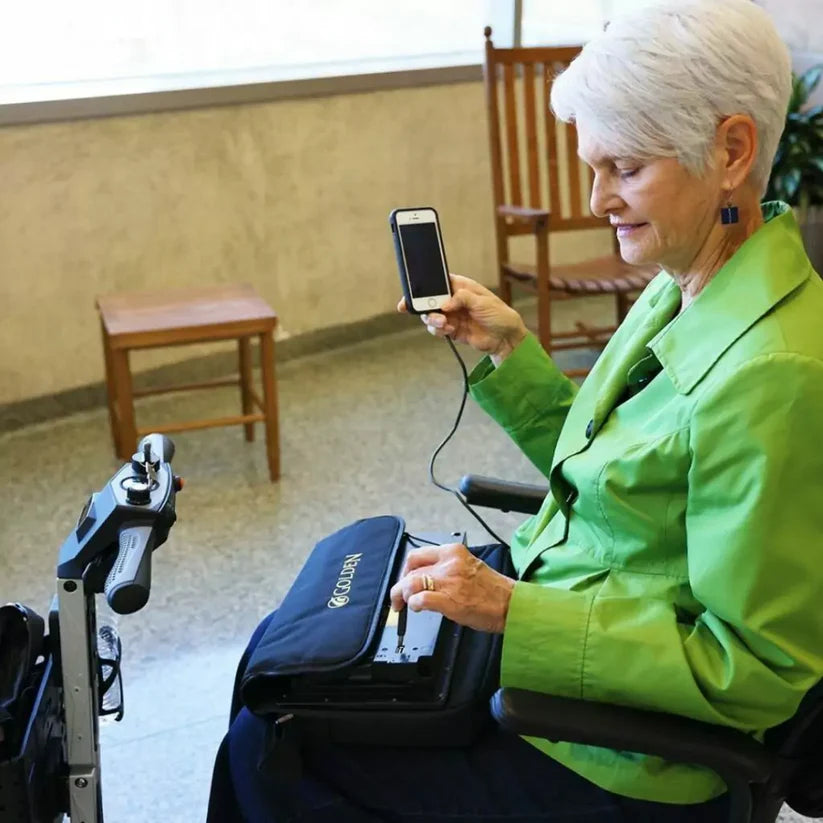 Senior woman using Golden Technologies Buzzaround CarryOn mobility scooter with smartphone in indoor setting