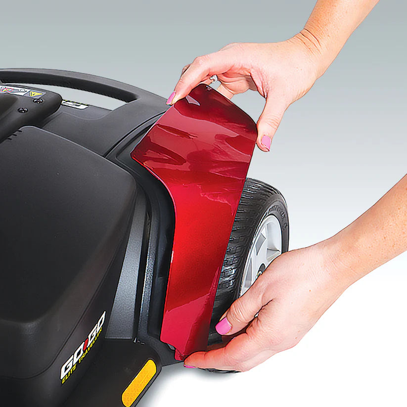 Hands detaching red panel from Pride Mobility Go Go Elite Traveller 3-Wheel scooter near rear wheel